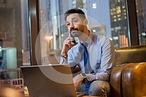 Portrait of handsome young business man with laptop talking on mobile phone in modern office.