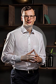 Portrait of a Handsome Young Businessman Standing Against Gray Wall Looking at the Camera with Arms Crossing Over her Stomach.