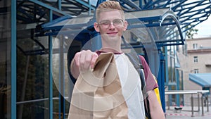 Portrait of handsome young Caucasian courier looking at camera stretching food delivery package smiling. Front view