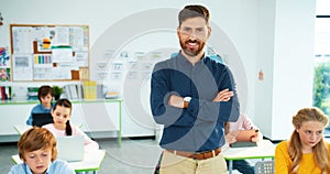 Portrait of handsome young Caucasian male tutor standing in classroom looking at camera and smiling. Children using