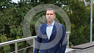 Portrait of handsome young classy man in suit walking outdoors in city. Caucasian confident successful businessman walks