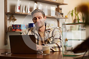 Portrait of handsome young digital nomad, man working in cafe on laptop, looking happy and pleased with his online