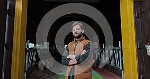 Portrait of a handsome young farmer in shirt and in orange vest looking at camera in background of dairy farm