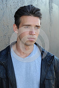 Portrait of a handsome young fashion man leaning on a gray wall while looking away from the camera