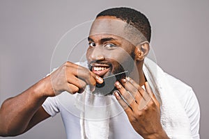 Portrait of handsome young african american black man combing his beard in bathroom. Isolated over grey background photo