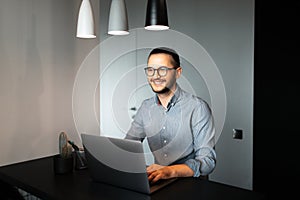 Portrait of handsome young happiness man, working home at laptop. Wearing eyeglasses and t-shirt. Background of grey wall