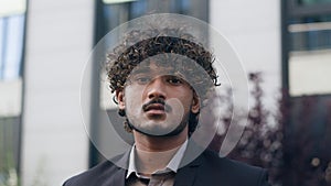 Portrait of handsome young Indian Arabian businessman standing outdoors urban outside looking at camera serious in city