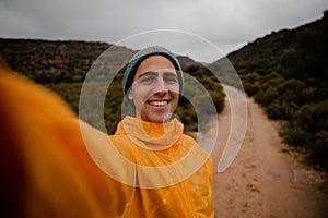 Portrait handsome young male hiker smiling at camera after steep hike on gravel mountain trail in cold cloudy weather