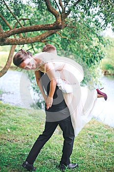 Portrait of a handsome young man carrying attractive woman on his back outdoors . Fun couple. Bride and gr