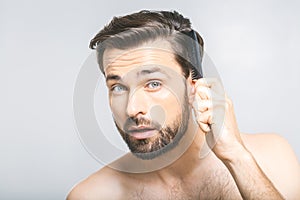 Portrait of handsome young man combing his hair in bathroom. Isolated over grey background