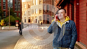 Portrait of handsome young man with dreadlocks dialing call on mobile phone, talking on modern city street. Positive