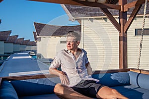 Portrait of handsome young man in expensive shirt at the swing at the tropical island luxury resort