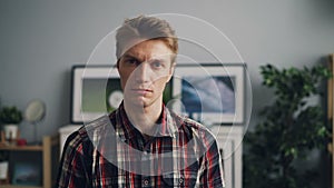 Portrait of handsome young man looking at camera with unhappy face wearing bright checkered shirt standing in modern