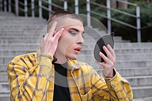 Portrait of a handsome young man  looking at his wrinkles in front of a mirror  wearing black eyeshadow  holding a makeup brush