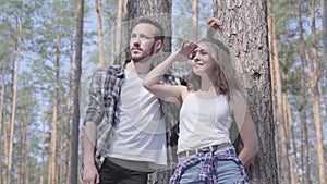 Portrait of handsome young man and pretty woman looking away standing in the pine forest. Concept of camping. Leisure