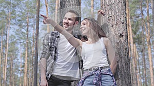 Portrait of handsome young man and pretty woman looking away standing in the pine forest. Concept of camping. Leisure