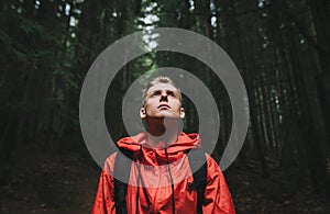 Portrait of a handsome young man in a red jacket stands in the evening forest with his head up, looking with a serious face.