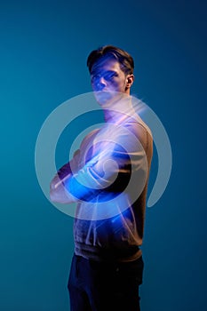 Portrait of handsome young man in stylish clothes posing with serious expression over blue background with mixed neon