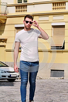 Portrait of handsome young man with sunglasses is posing and walking on urban city street. Male model photo-shoot outdoors.