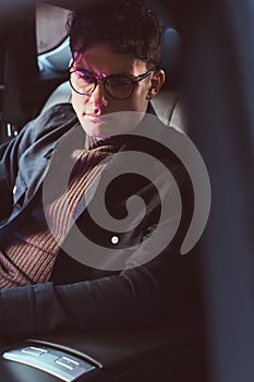 A handsome young man wearing glasses sitting in the back seat of the car.