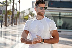Portrait of handsome young man wearing sunglasses and white tshirt, posing on city street background. Casual style
