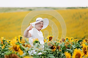 Portrait of a handsome young man in a white woman`s hat in a field with sunflowers. Man is having fun outdoors. copy space.