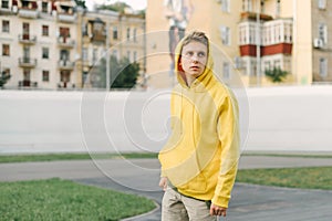 Portrait of a handsome young man in a yellow hoodie standing on the sports field and posing at the camera on an urban background.
