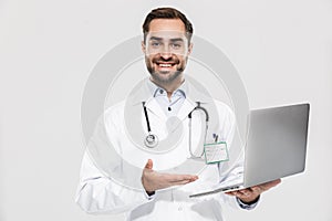 Portrait of handsome young medical doctor with stethoscope working in clinic and holding laptop