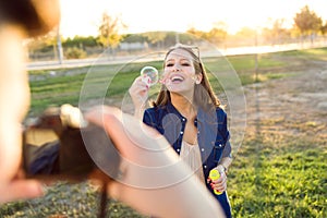 Handsome young man taking photo of his girlfriend making soap bubbles in the park.