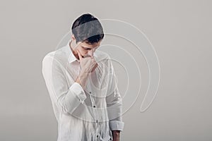 Portrait of handsome young pensive man in white shirt on gray ba