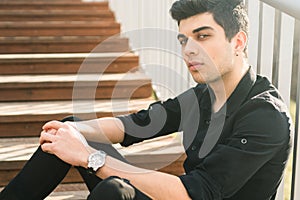 Portrait of a handsome young successful male brunette of a Turkish Mediterranean race sitting on the urban stairs in a