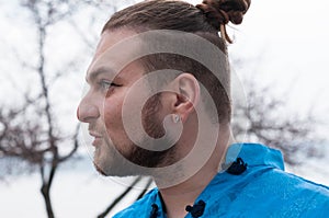 Portrait of hansome bearded man with hair bun and make up looking away and speaking