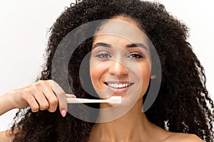 Portrait of happy 20s African-American woman with great smile standing over white background and brushing teeth with a