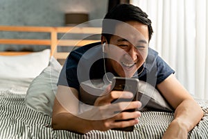 Portrait of happy 30s aged Asian man in casual clothing making facetime video calling with smartphone at home. He`s