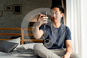 Portrait of happy 30s aged Asian man in casual clothing making facetime video calling with smartphone at home. He`s