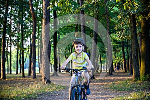 Portrait of happy active teenage boy in safety helmet relaxing after school riding his bike in beautiful park on sunny autumn day