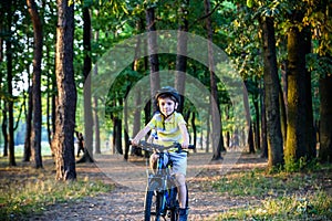 Portrait of happy active teenage boy in safety helmet relaxing after school riding his bike in beautiful park on sunny autumn day