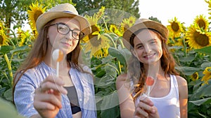 Portrait of happy adolescents with sweet lollipops in hands smiling on background of yellow field with sunflowers