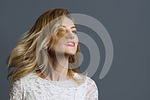Portrait of happy adult blonde woman spinning her head, grey background