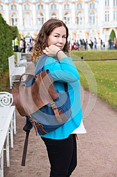 Portrait of happy adult woman throwing her leather bag on shoulder, looking at camera, standing in urban park