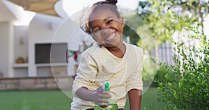 Portrait of happy african amercian girl watering plants holding spray bottle in garden