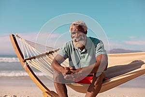 Portrait of happy african american bearded senior man sitting on hammock against blue sky in summer