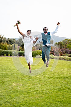 Portrait of happy african american couple holding hands and jumping during wedding