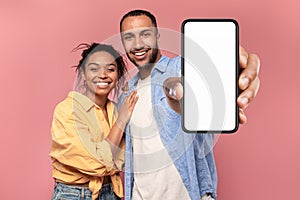 Portrait of happy african american couple presenting cellphone with mockup, promoting app or website