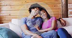 Portrait of happy african american couple sitting on sofa in log cabin, slow motion