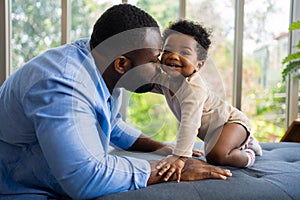 Portrait Of Happy African American Dad With Cute Little Baby Girl on couch at home in the living room, caring father smiling and