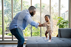 Portrait Of Happy African American Dad With Cute Little Baby Girl on couch at home in the living room, caring father smiling and