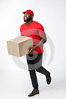 Portrait of Happy African American delivery man in red cloth walking to send a box package to customer. Isolated on Grey