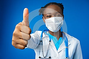 Portrait happy African American female doctor showing ok sign in blue studio