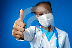 Portrait happy African American female doctor showing ok sign in blue studio